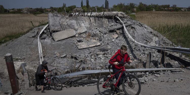 Dos adolescentes pasan en bicicleta por un puente destruido cerca de Orihiv, Ucrania, el 5 de mayo de 2022.(Evgeniy Maloletka / Associated Press)